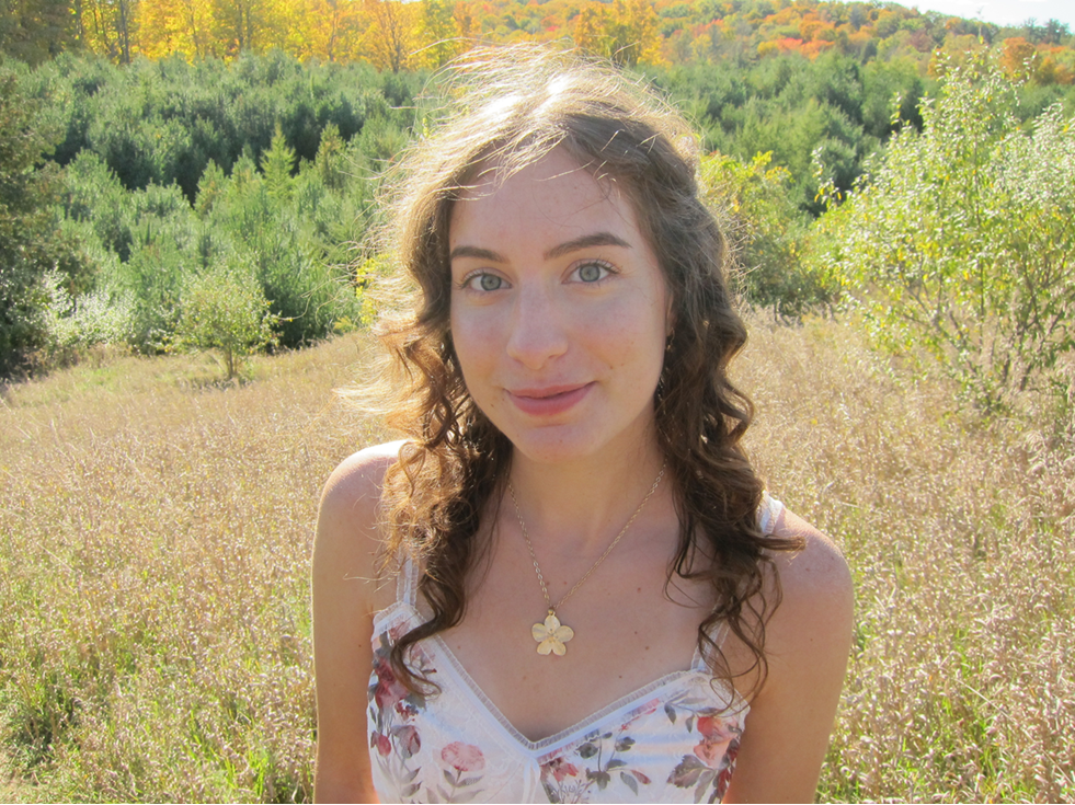 Woman standing in a field with trees and foliage in the background