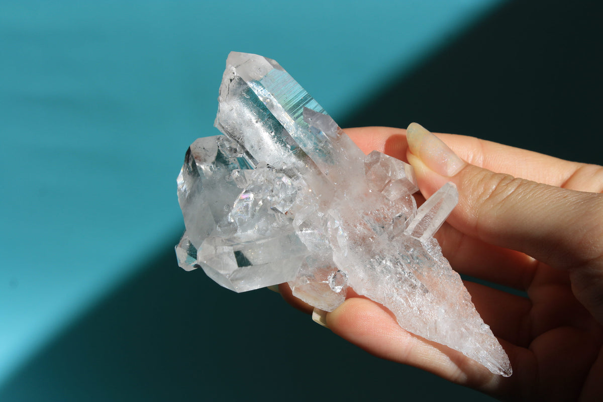 Clear crystal held in a hand against a teal background