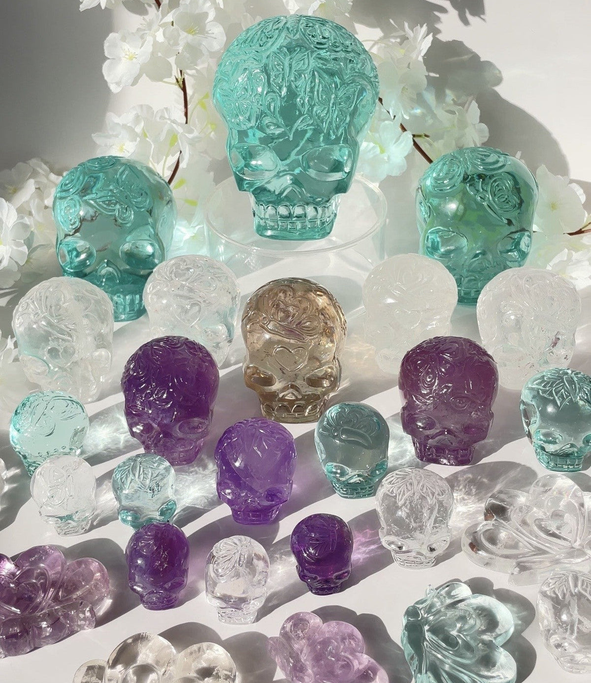 Colorful crystal skulls on a white surface with white flowers in the background