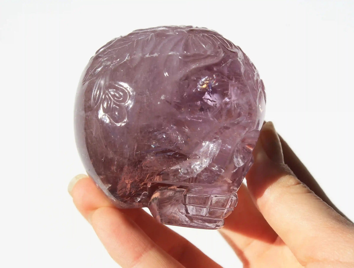 A hand holding a carved purple crystal skull against a plain white background.
